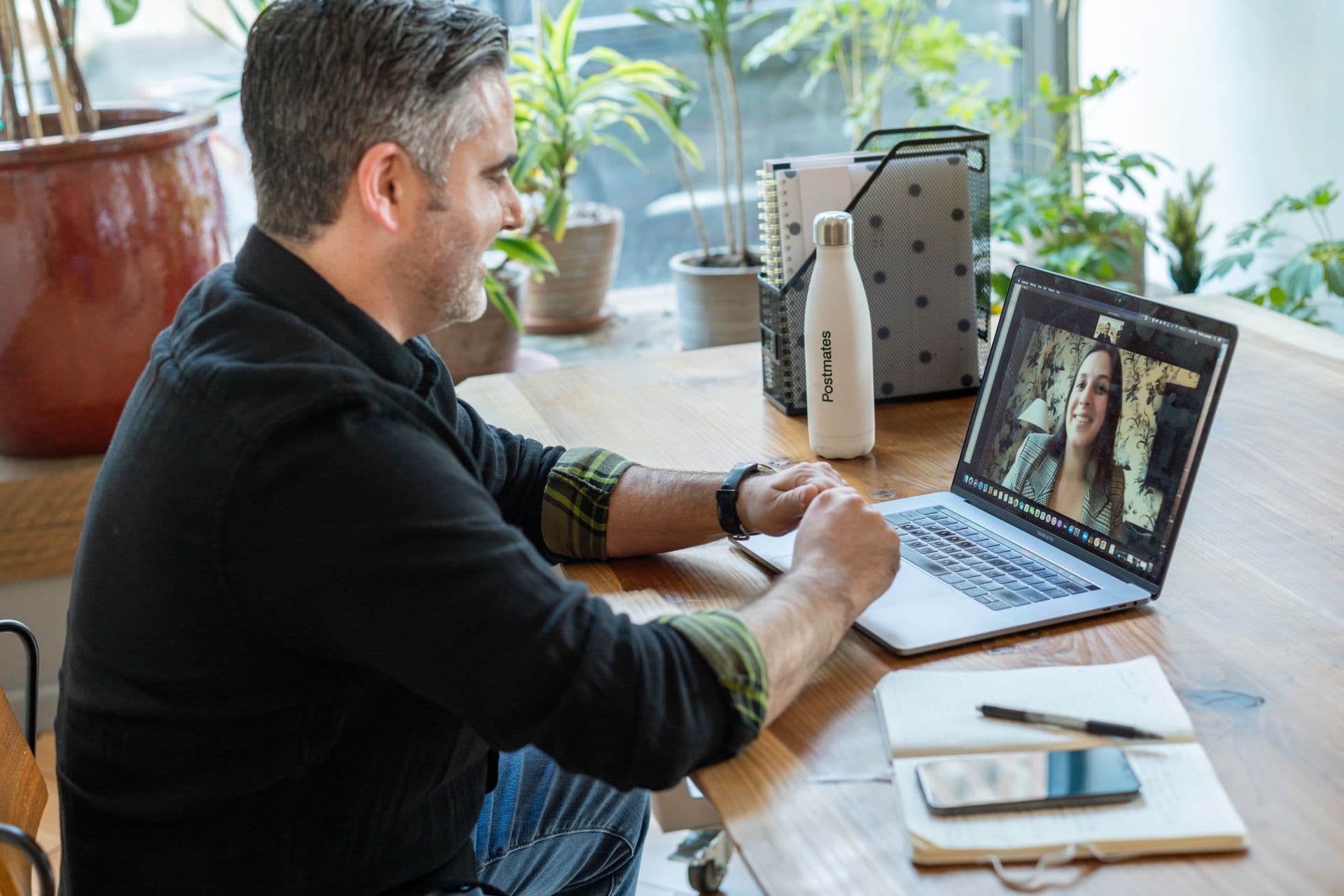 A smiling man on a video call with a colleague from his plant-filled home office